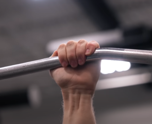 Čovekova šaka koja drži pravu šipku na lat mašini, koristeći hvat bez palca, tj. thumbless grip.